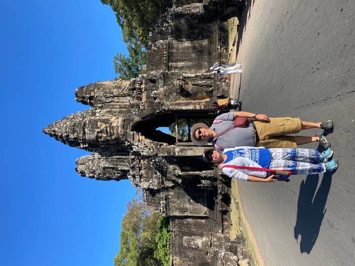Couple posing on a roadway before the towering stone South Gate of Angkor Thom under a clear blue sky.