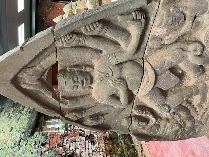 Ancient sandstone bas-relief of a multi-armed Hindu deity inside a brick temple structure