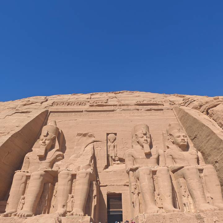 Low-angle view of the colossal seated statues and hieroglyphs of Abu Simbel against a flawless blue sky.