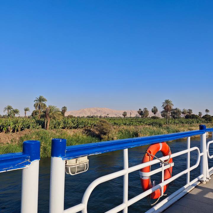 View from a Nile cruise boat of lush banana plantations with desert hills beyond under a clear sky.