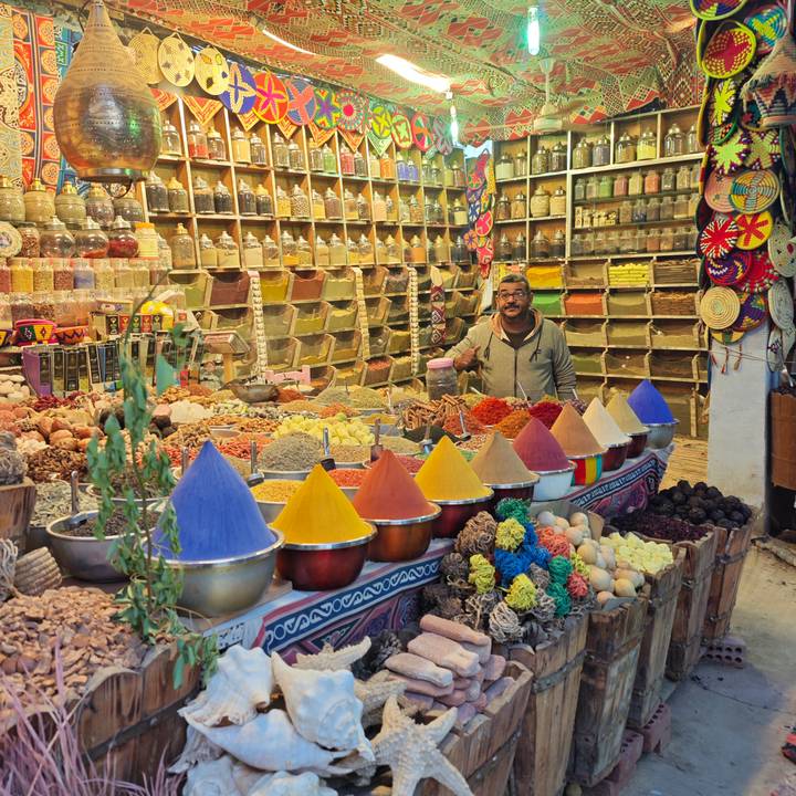 Vendor smiles behind pyramids of vividly coloured spices in a bustling Egyptian market stall.