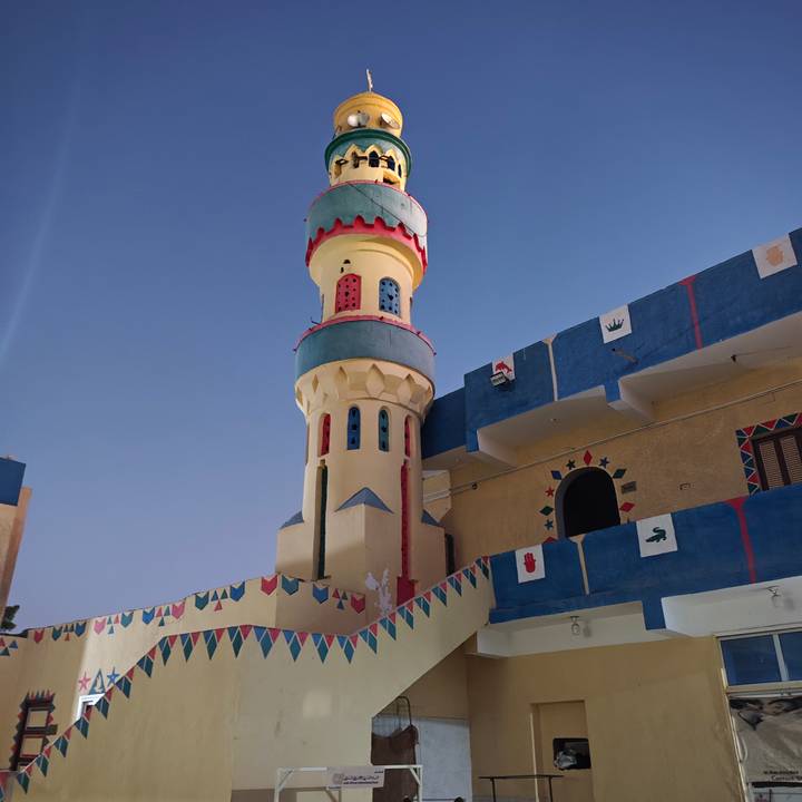 Colourful Nubian minaret with geometric motifs stands against a clear twilight sky.