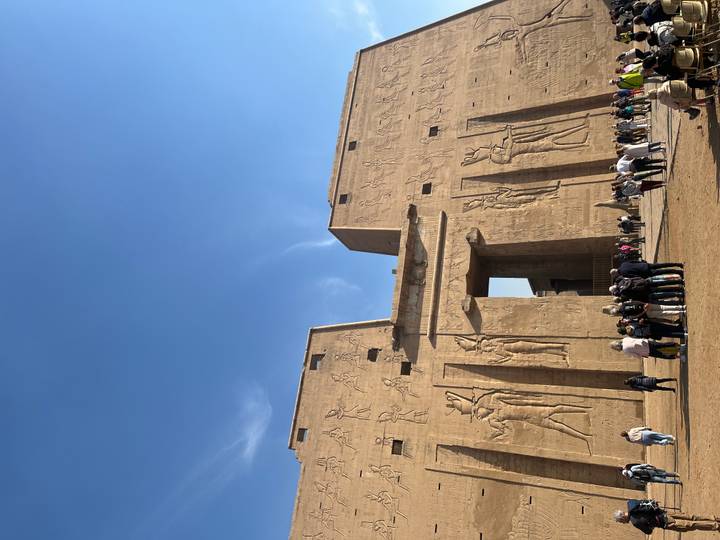 Grand pylon entrance of Edfu Temple adorned with reliefs, with groups of tourists below.