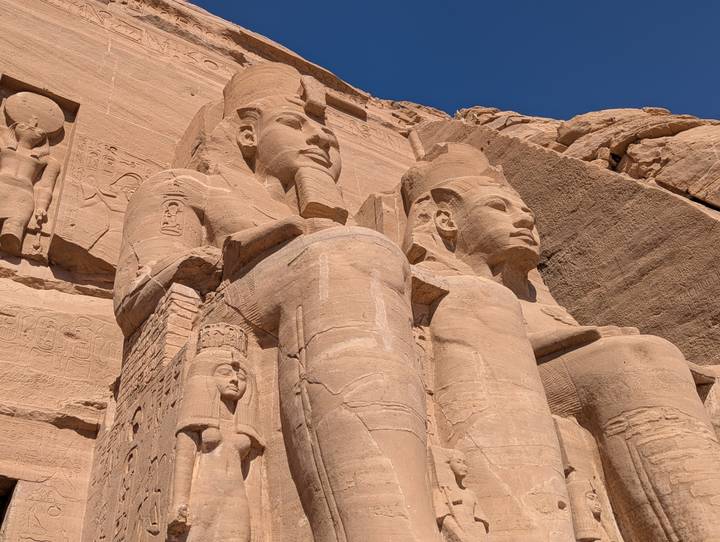 Close-up of two colossal seated statues carved into sandstone at Abu Simbel against a deep blue sky.