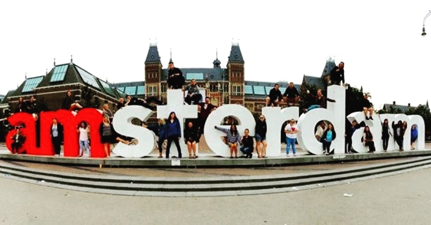 Personnes posant sur les lettres "I amsterdam" dans une zone urbaine animée.