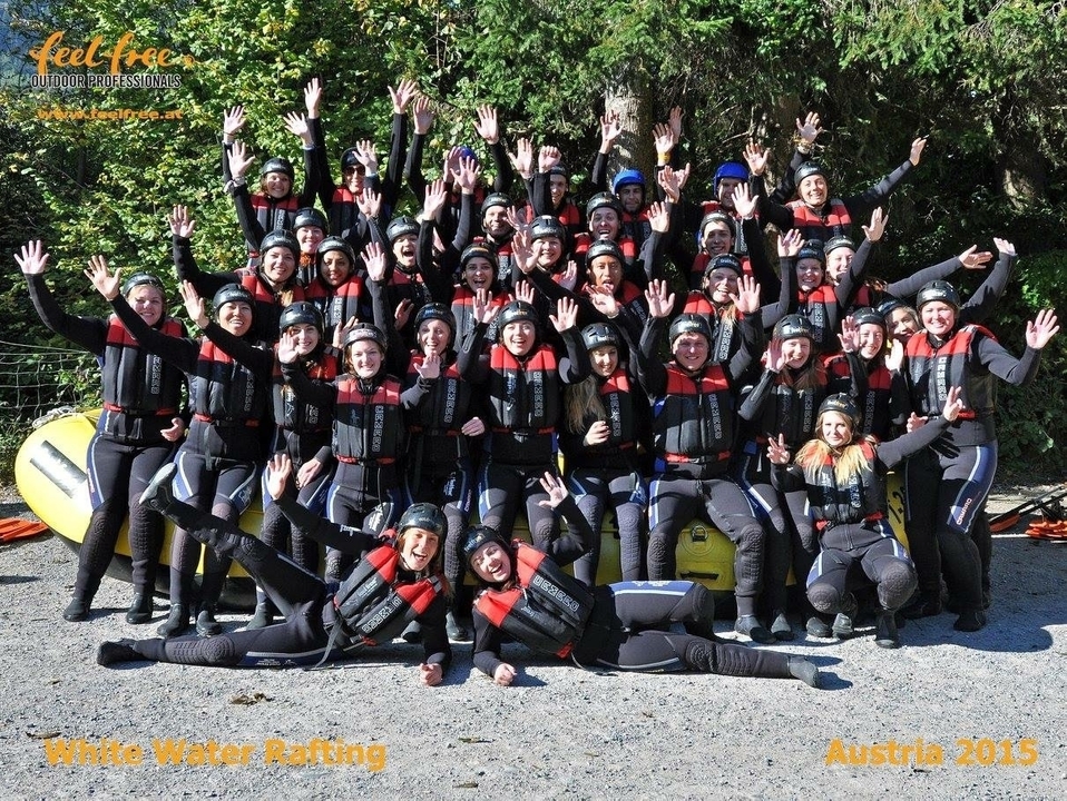 Groupe de personnes en combinaison de plongée posant avec enthousiasme devant un site de rafting.