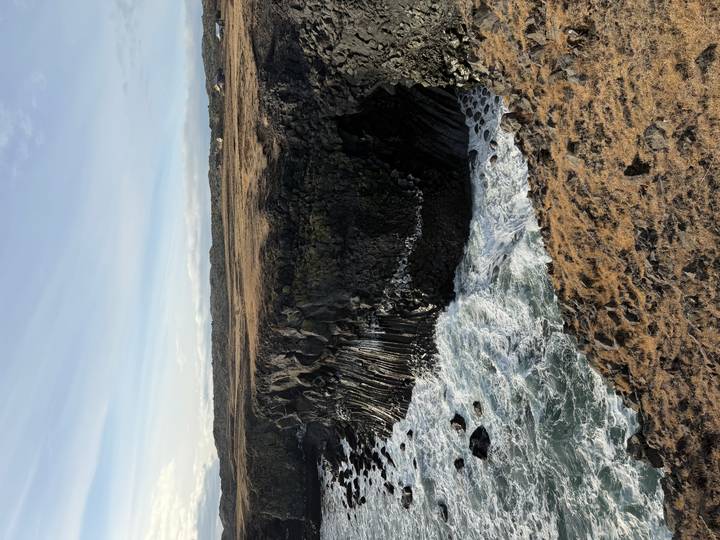 Rugged basalt sea cliffs battered by white surf along a barren Icelandic coast.