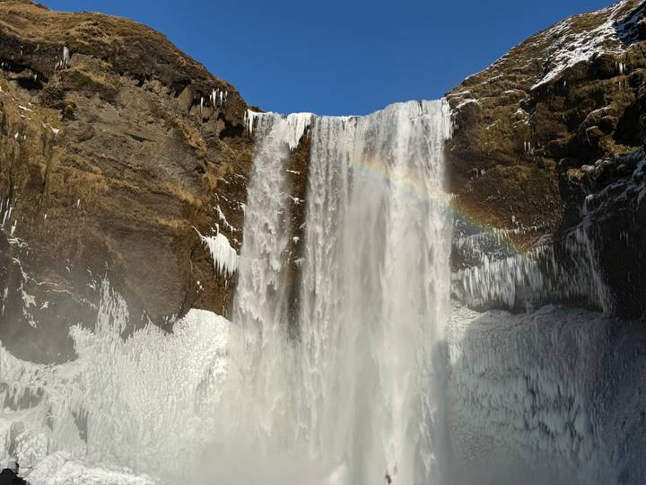 Powerful Skógafoss waterfall plunging over an icy cliff face with a rainbow arching through its mist.
