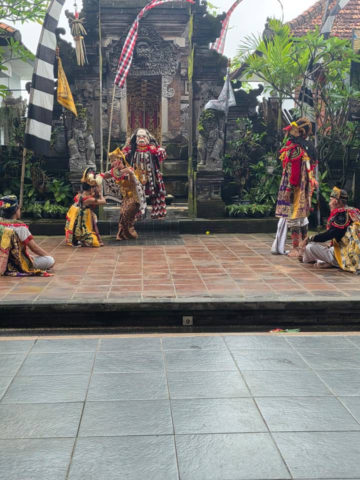 Scene from a Balinese dance drama with multiple actors in vivid traditional dress interacting on stage.