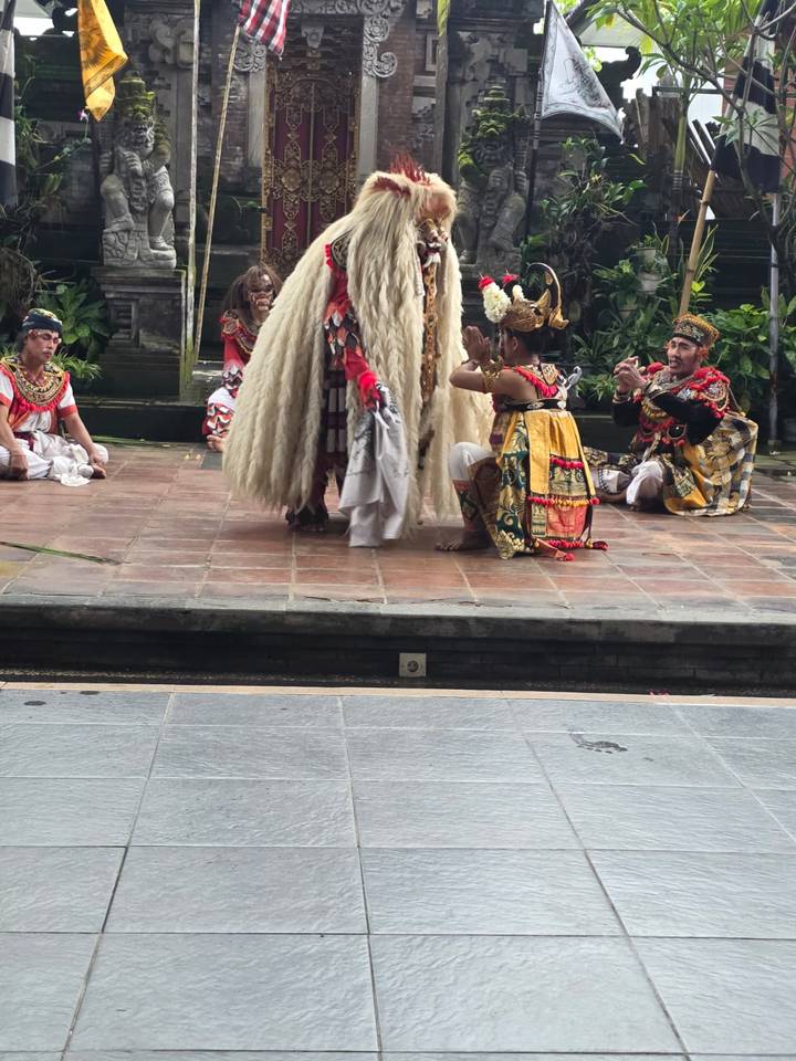 Close view of Balinese dancers kneeling before a shaggy Barong character on a stone stage.