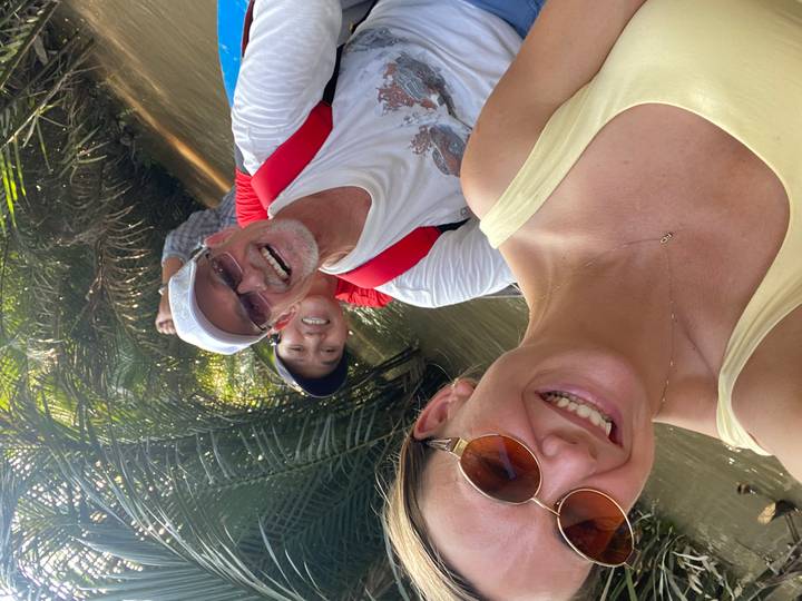 Three friends laughing while paddling through narrow Mekong Delta waterways among palm trees.