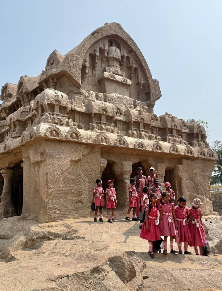 School children pose in matching uniforms beside ancient rock-cut architecture at Mahabalipuram.