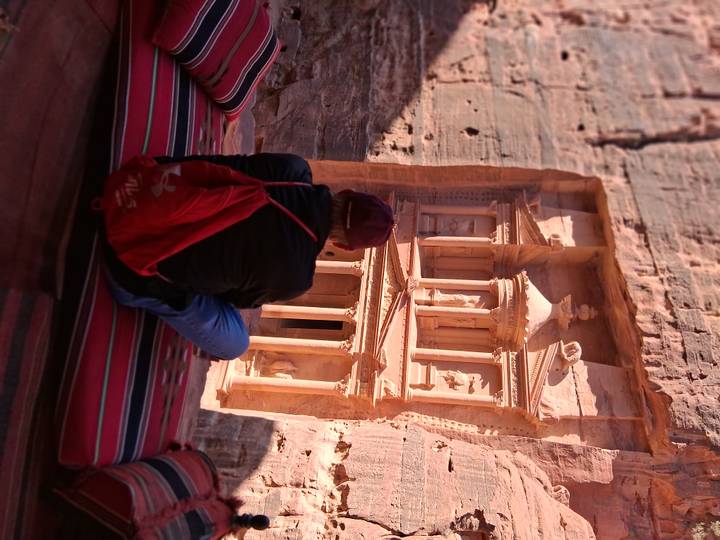 Traveler seated on colorful cushions gazes at the iconic Treasury carved into the rose-red cliffs of Petra.