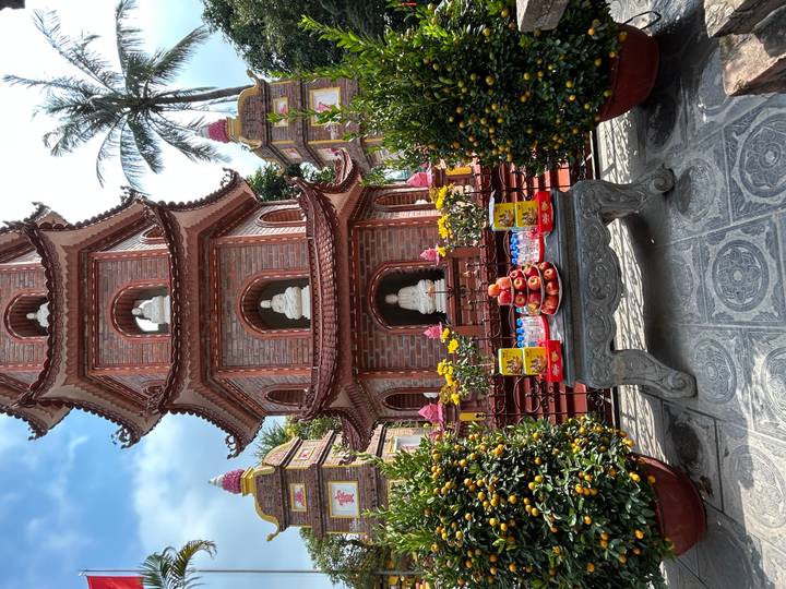 Brick pagoda tower with Buddha statues and festive fruit offerings arranged on a stone table in the courtyard.