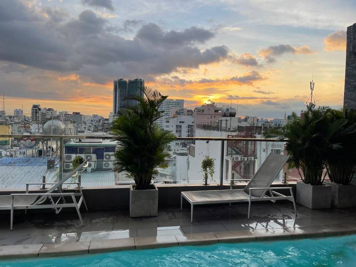 City-rooftop terrace with lounge chairs overlooks Ho Chi Minh skyline at sunset.