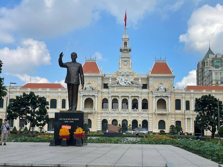 Statue of Ho Chi Minh stands before the ornate French-colonial City Hall in Ho Chi Minh City on a sunny day.