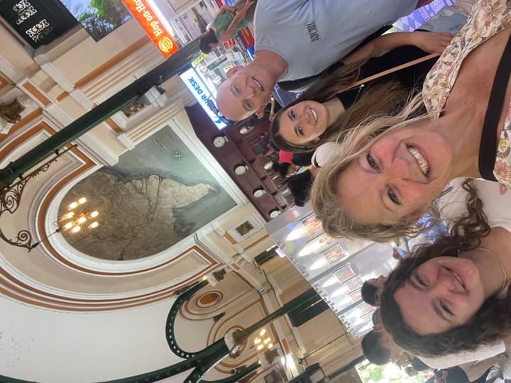 Smiling family selfie inside the Saigon Central Post Office beneath its grand arched map ceiling.