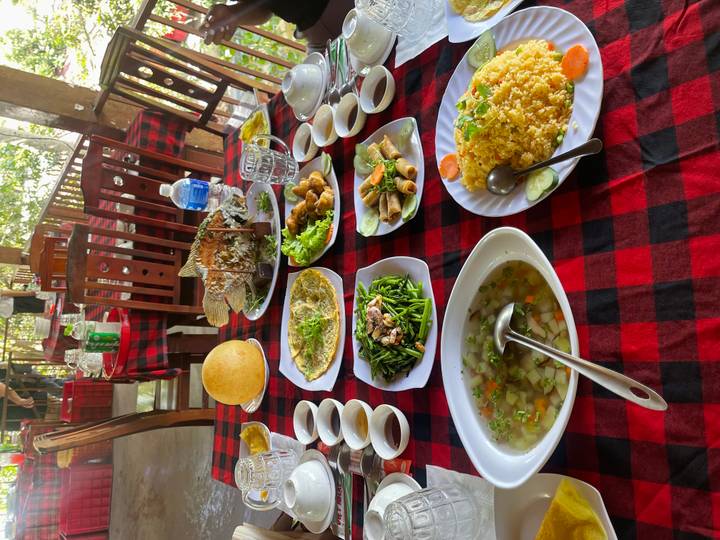 A colourful Vietnamese feast laid out on a checkered tablecloth inside a rustic open-air restaurant.