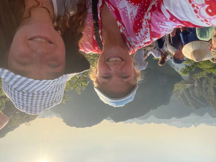 Mother and daughter smile at a scenic mountain and river vista bathed in warm late-afternoon light.