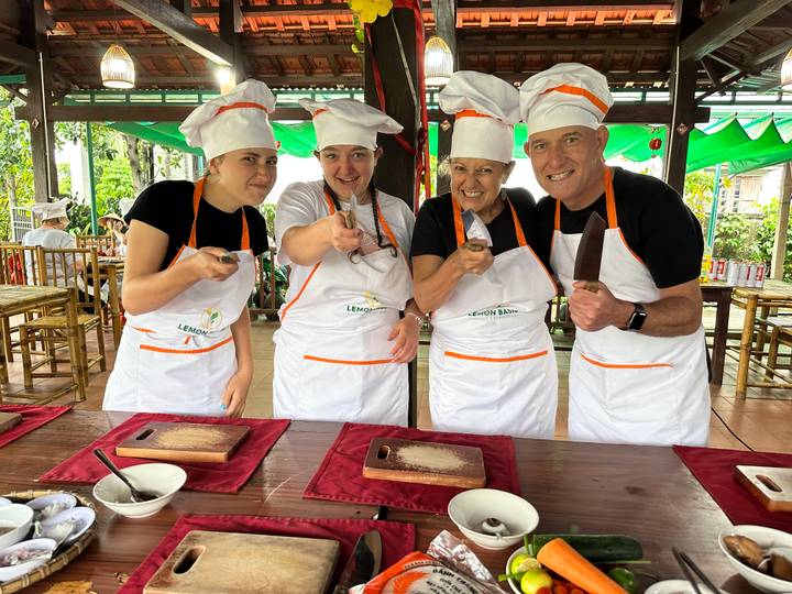 Four participants in chef hats and aprons enthusiastically pose during a Vietnamese cooking class.