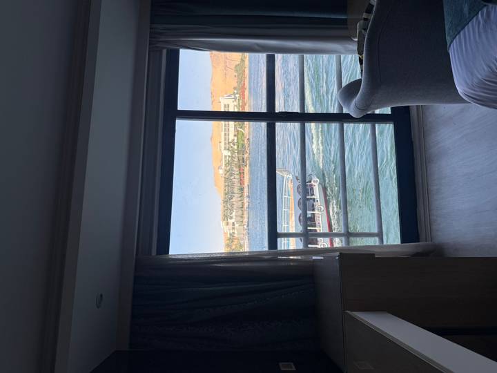 View from a hotel cabin window overlooking passing boats on a wide river under clear skies