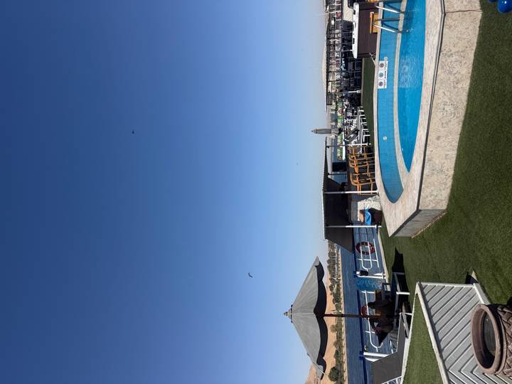 Sunny rooftop pool deck of a cruise ship with lounge areas overlooking desert river scenery