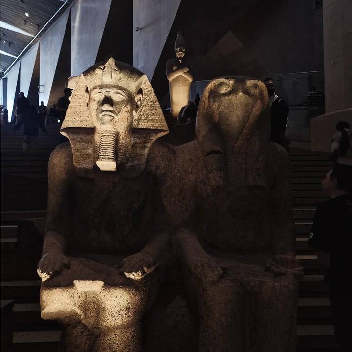 Dimly lit museum hall displaying twin ancient statues with visitors in the background