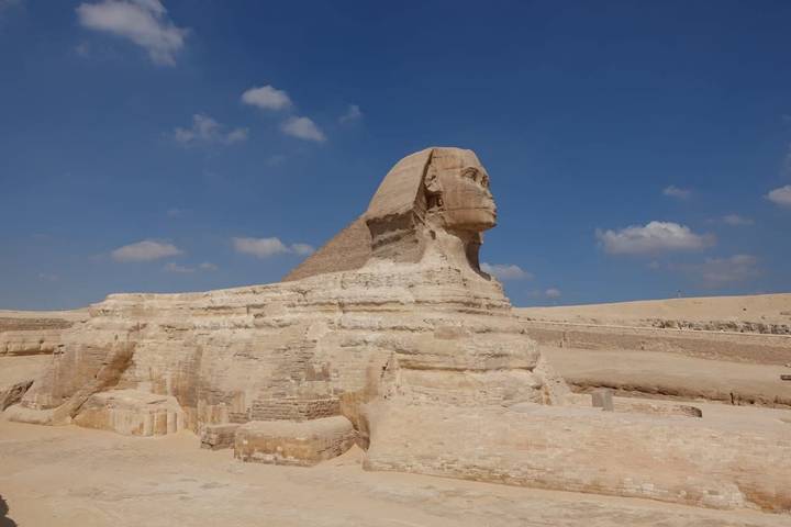 Side profile of the Great Sphinx against a blue sky with scattered clouds
