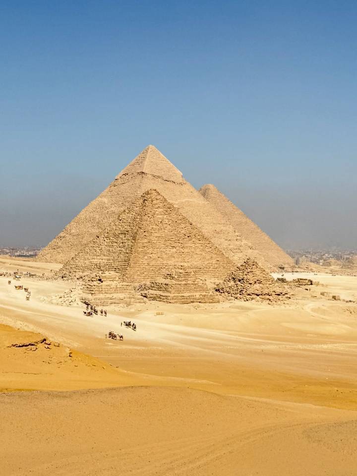 Telephoto view of the Great Pyramid against hazy sky with small tourist caravans below