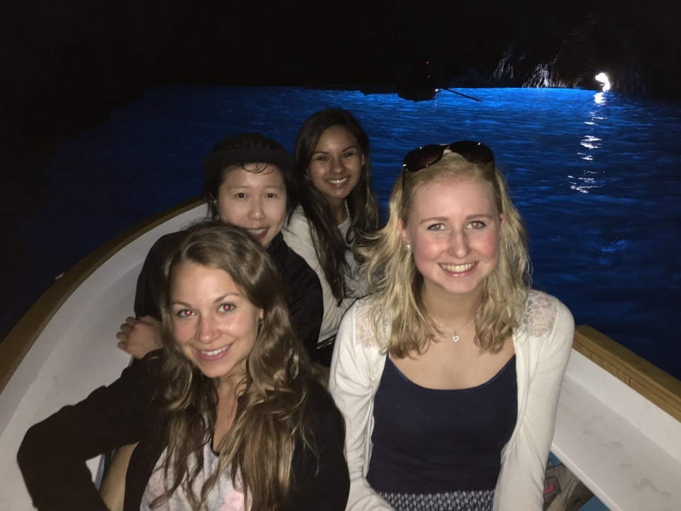 Quatre personnes sur un bateau à l'intérieur d'une grotte aux eaux lumineuses.