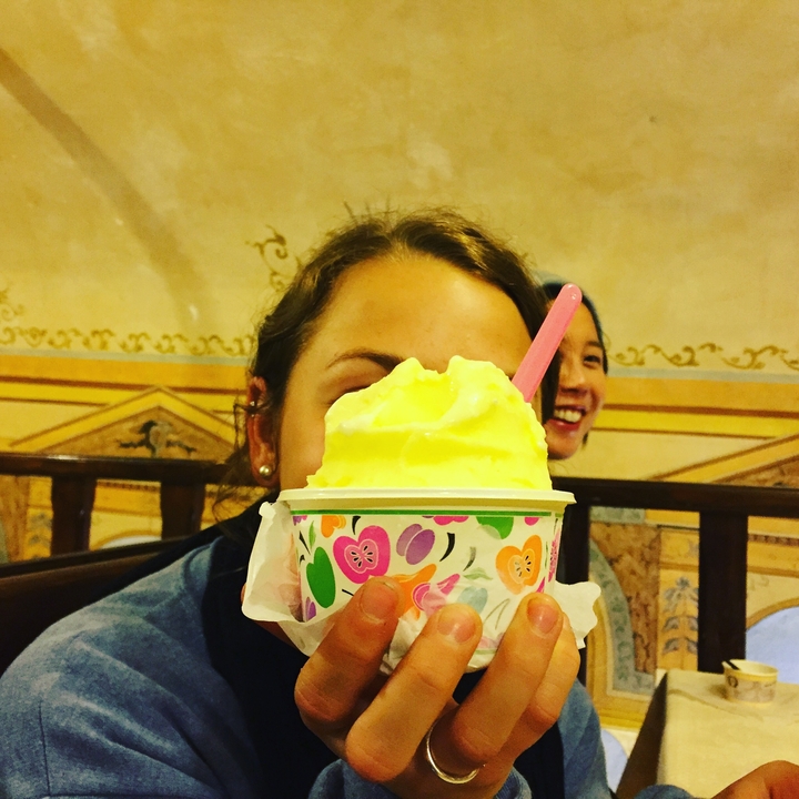 Une personne tenant un gelato devant son visage avec une autre personne souriant en arrière-plan.