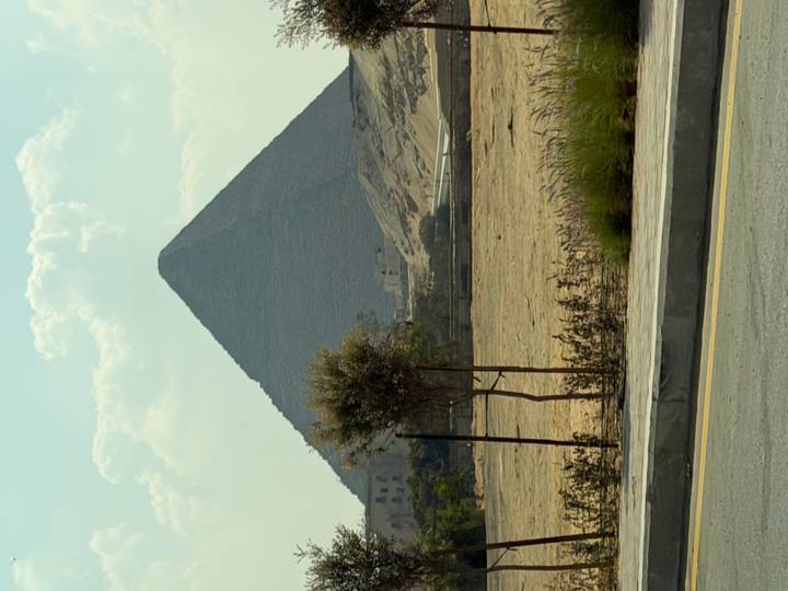 Side view of a pyramid rising above the desert with sparse vegetation and road in foreground.