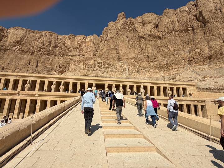 Tourists walking up the central ramp toward Hatshepsut Temple carved into desert cliffs.