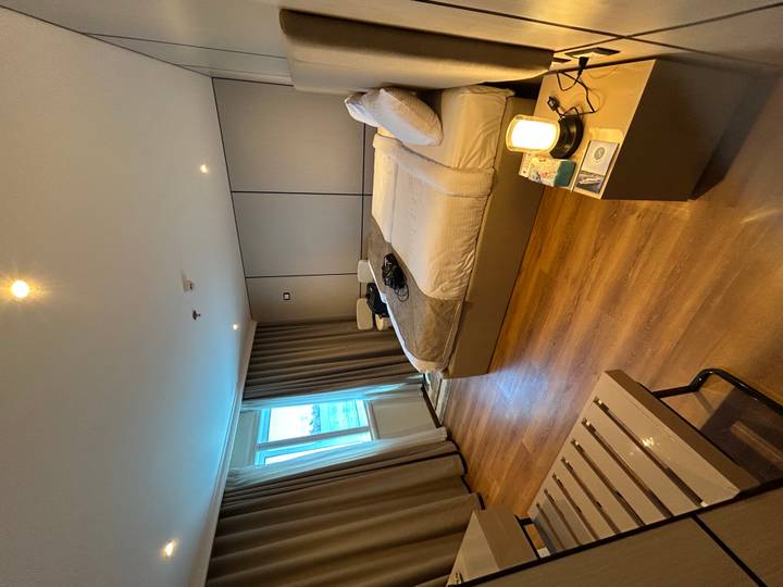 Modern hotel room with large bed, wooden floor, window and warm lighting.