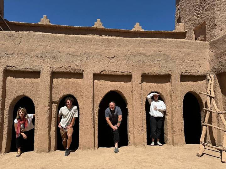 Travellers posing inside the small arched doorways of an adobe kasbah structure.