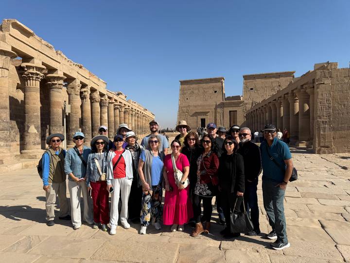 Tour group lined up between massive sandstone colonnades of an ancient temple complex.