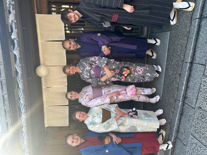 Four travelers dressed in elegant kimonos standing outside a traditional wooden machiya in Kyoto.