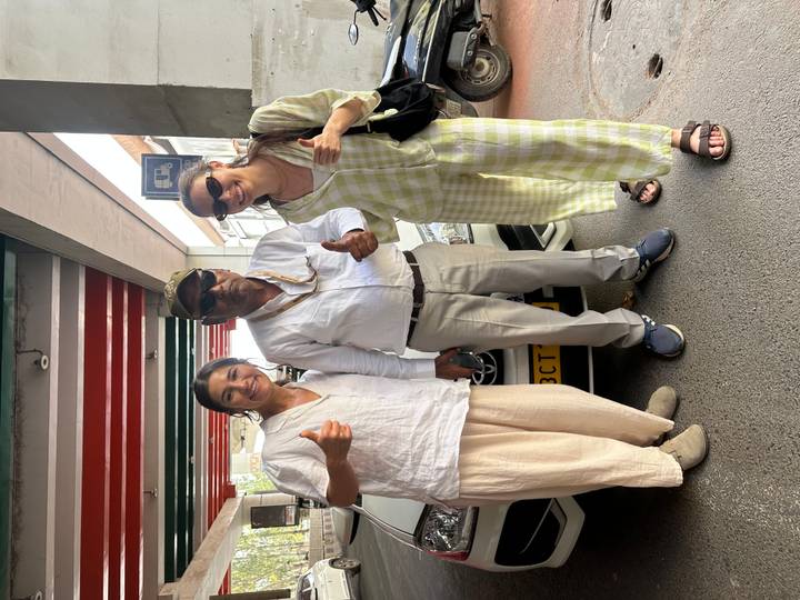 Two tourists give thumbs up beside their driver under a parking shelter.