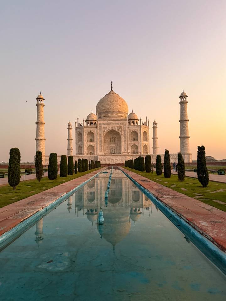 Iconic Taj Mahal at sunrise reflected symmetrically in the long pool leading to the mausoleum.