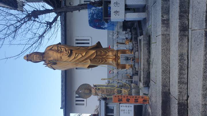 Tall golden Kannon statue at a Japanese temple surrounded by smaller figures and stone steps.