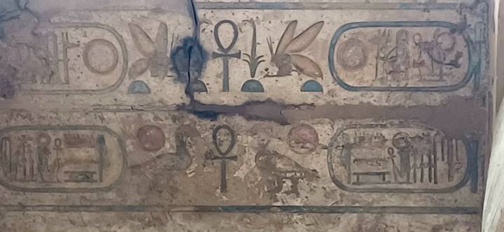 Weathered wall section with faded ankh and cartouches among damaged plaster