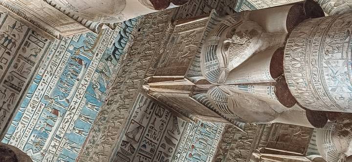 Colorful ceiling reliefs and ornate lotus-cap capitals inside an ancient Egyptian temple.