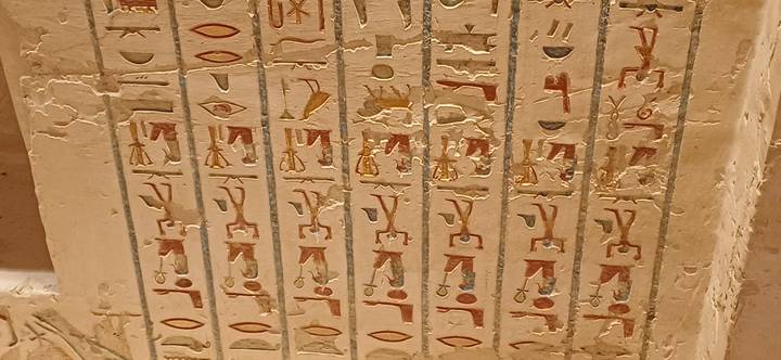 Close-up of painted hieroglyphic columns on a tomb wall with vivid reds and yellows.