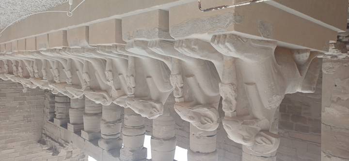 Row of ram-headed sphinxes lining the entrance corridor of an ancient sandstone temple.