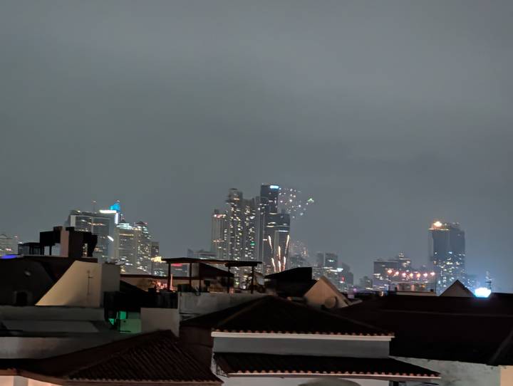 Nighttime city skyline with illuminated high-rise buildings beyond dark rooftops.