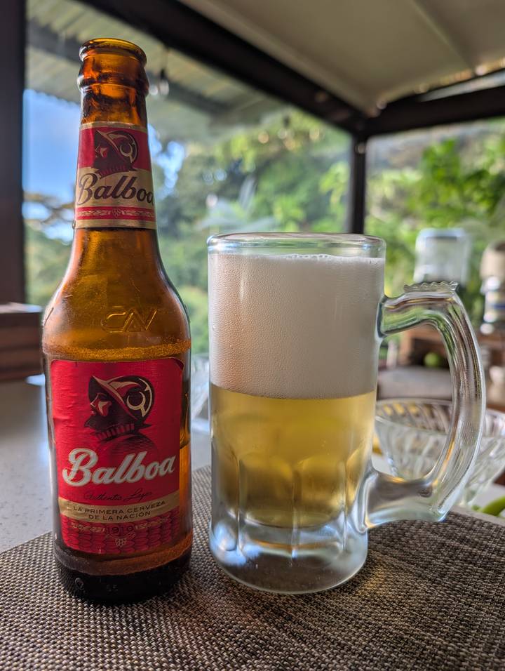 Close-up of a frothy pint glass beside a Balboa beer bottle on a table.