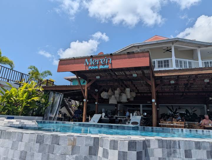 Poolside view of Merén Pool Café, a wooden beachfront venue with hanging basket lamps.