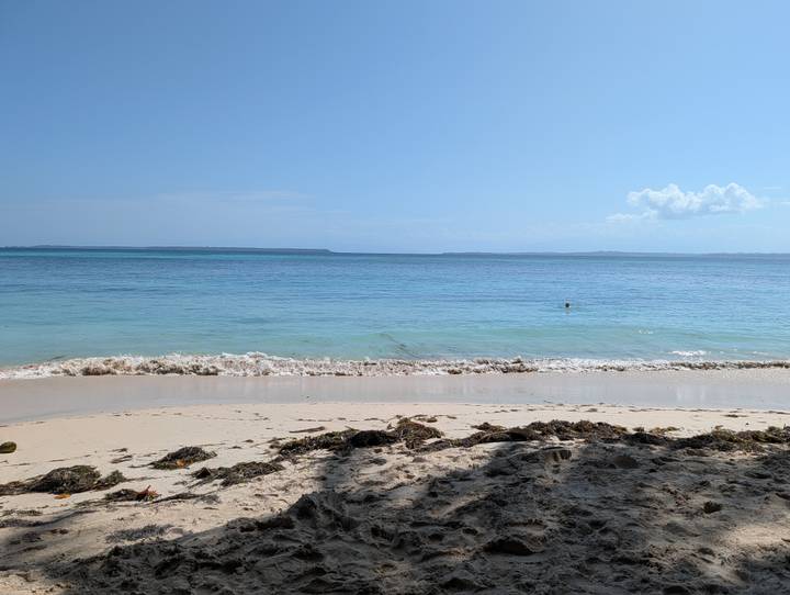 Quiet sandy beach with gentle turquoise waves under a clear blue sky.