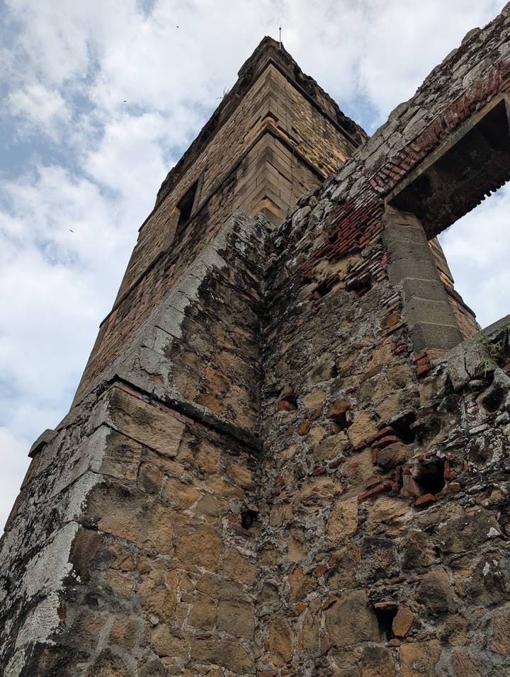 Upward perspective of an aged stone tower wall with weathered bricks against a cloudy sky.