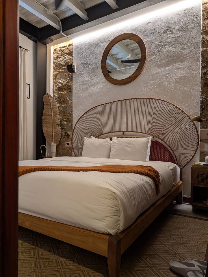 Stylish hotel room with rattan headboard, crisp white bedding and warm accent throw.